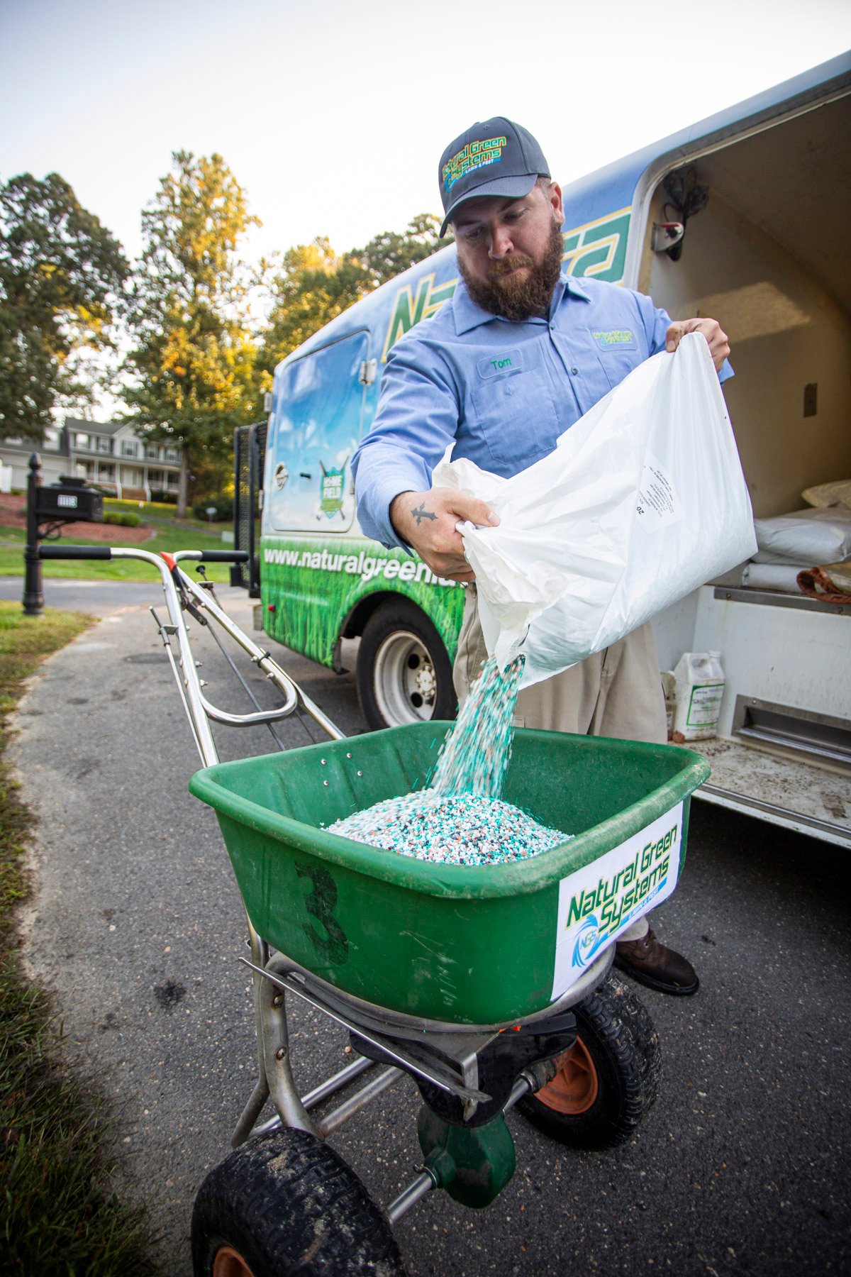 lawn care technician pours fertilizer into spreader