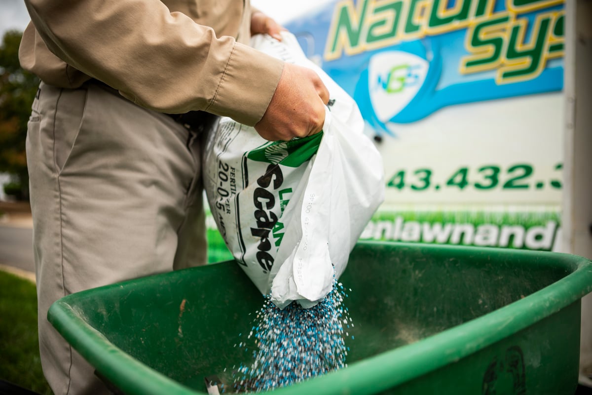 lawn technician pours fertilizer in spreader
