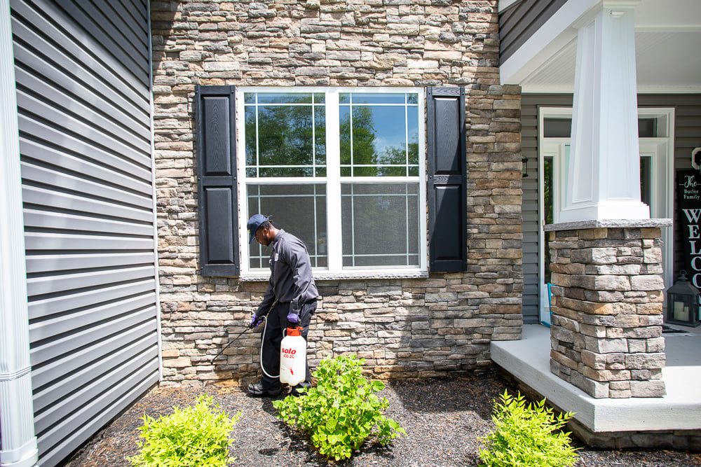 pest control technician sprays exterior of home